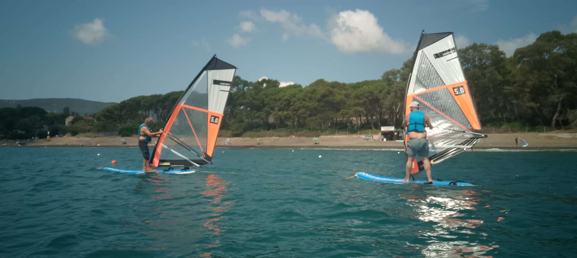 Due windsurfer con vela arancione nelle acque cristalline di Margidore, Lacona